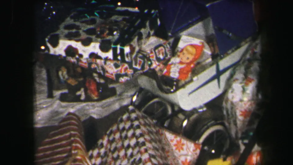 1971 Lynbrook Christmas gift display with wrapped packages, a doll, toy carriage and patterned textiles in an indoor setting.