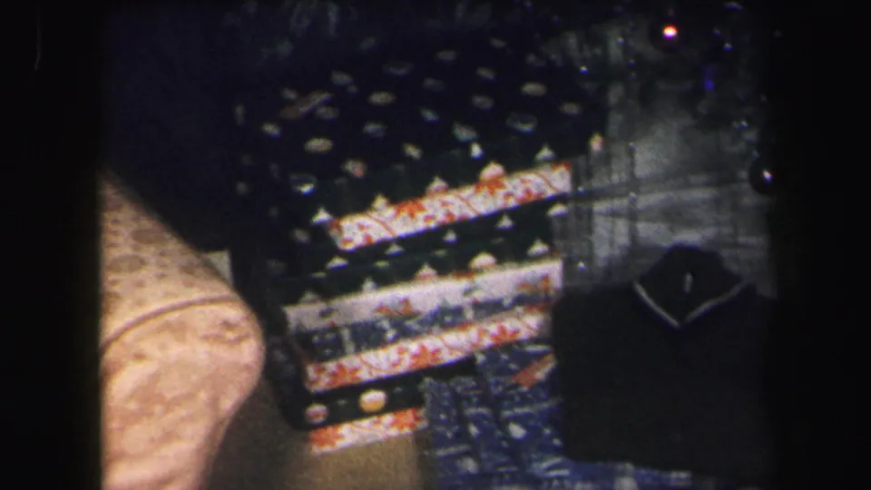 Close 1971 home-movie view of stacked Christmas gifts, patterned wrapping paper and a dark package on the table.