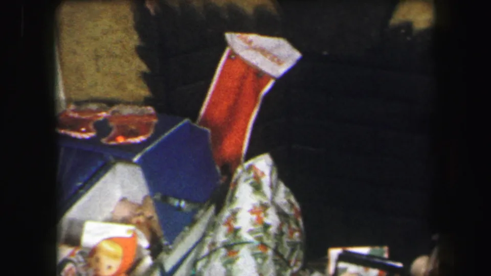 1971 Lynbrook frame with a red stocking, blue-and-white gift box, patterned fabric, and low-light 8mm home interior detail.