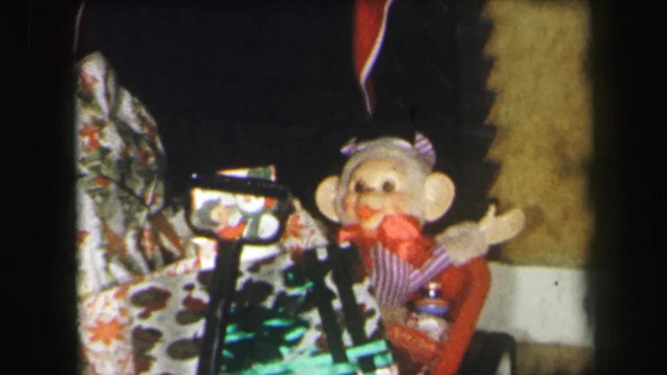 1971 Lynbrook holiday frame with a sock monkey, red-and-white stockings, wrapped presents, and toy parts near the fireplace.