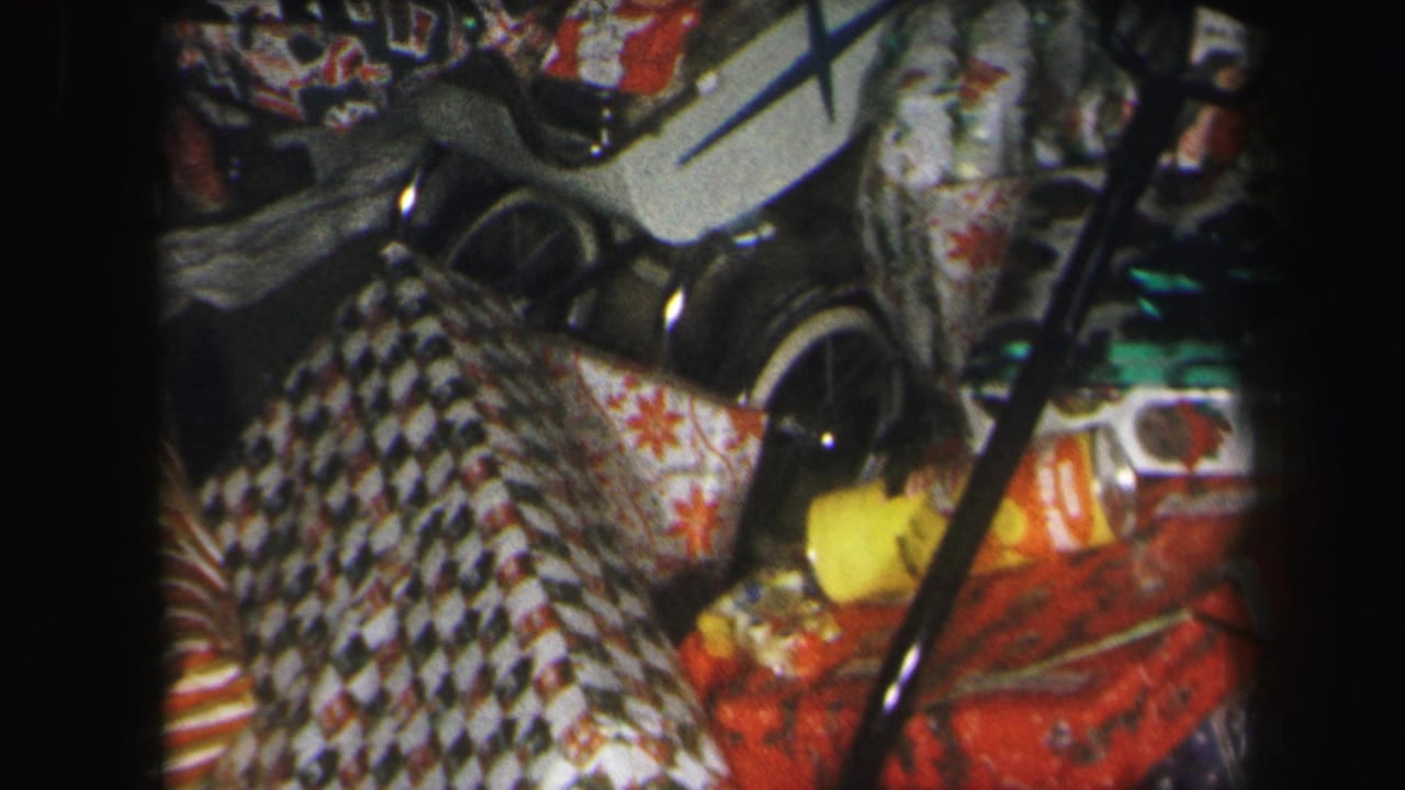 1971 Lynbrook home-movie frame showing wrapped Christmas presents, patterned paper, a white toy stroller, and a small doll near the tree.
