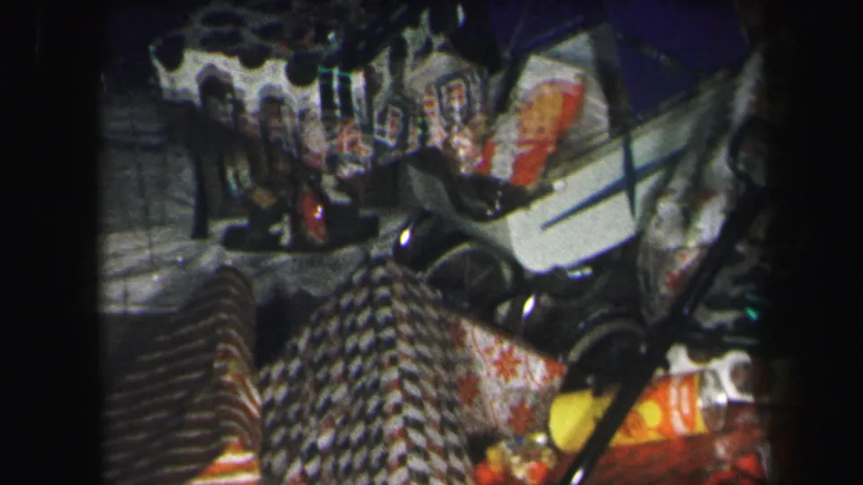 1971 Lynbrook holiday frame with a pile of wrapped gifts, toy stroller, doll, and patterned wrapping paper in grainy 8mm color.