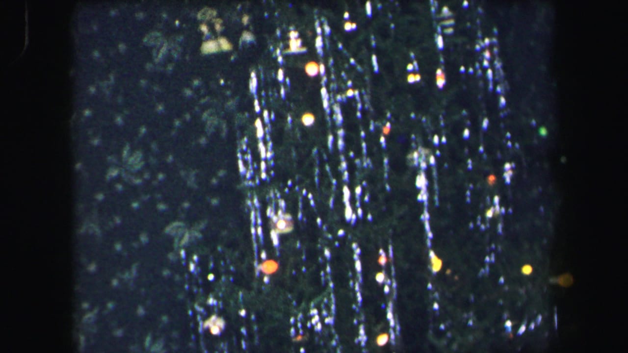 Decorated Christmas tree with tinsel, ornaments, and small colored lights in a dark room.