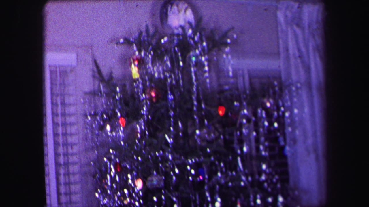 Tinsel-covered Christmas tree with colored lights inside a living room.