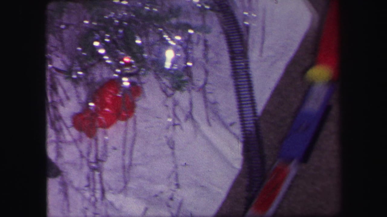 1971 Lynbrook home-movie frame showing Christmas tree decorations, tinsel, and part of a toy train track near the tree base.