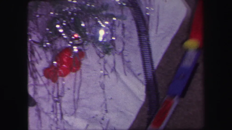 1971 Lynbrook home-movie frame showing Christmas tree decorations, tinsel, and part of a toy train track near the tree base.