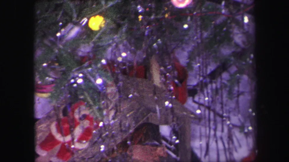 1971 Lynbrook home-movie frame showing a toy train beneath a decorated Christmas tree, with tinsel, ornaments, and a Santa figure nearby.
