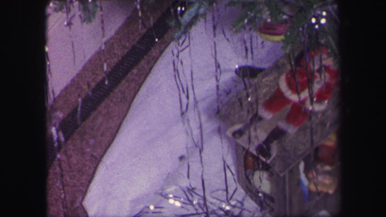 1971 Lynbrook home-movie frame showing a toy train track, Santa figure, tinsel, and holiday display beneath a Christmas tree.
