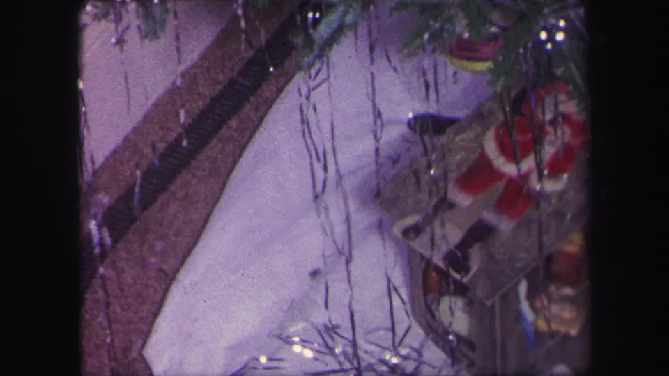 1971 Lynbrook home-movie frame showing a toy train track, Santa figure, tinsel, and holiday display beneath a Christmas tree.