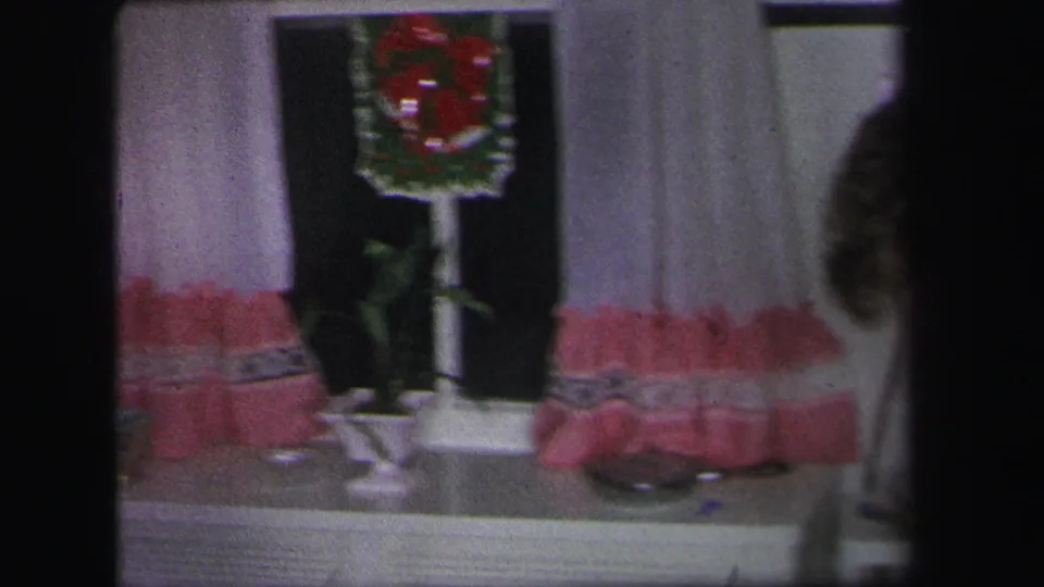 A curtained window in the Lynbrook home shows a red wreath decoration, with part of a person visible at the edge of the frame.