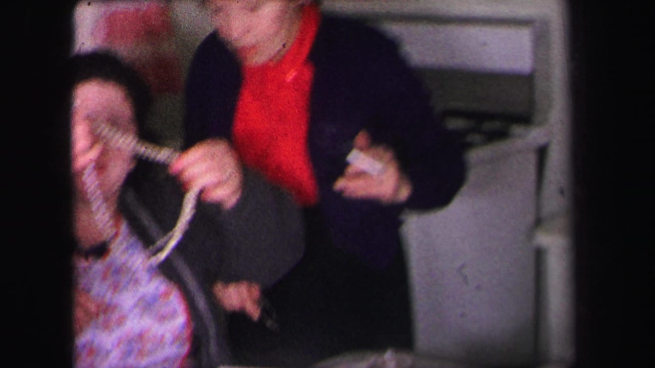 Women indoors examining a necklace near a kitchen or dining area.