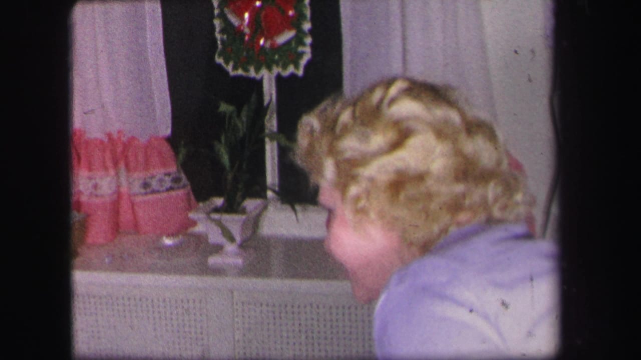 Blonde woman in a light blue top near a window with curtains and a wreath.