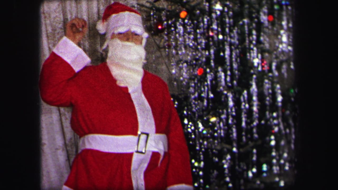 In a 1971 Lynbrook home movie, a child in a red Santa suit and white beard waves beside a decorated tinsel Christmas tree.
