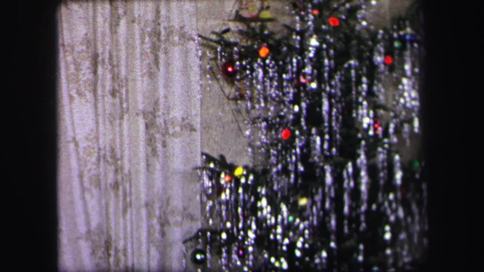 The camera holds on the lower tinsel Christmas tree and curtains, with holiday lights visible in the home interior.