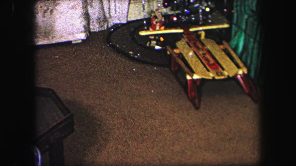 The camera pans across a Lynbrook Christmas interior toward a wooden sled near the tree and train track.