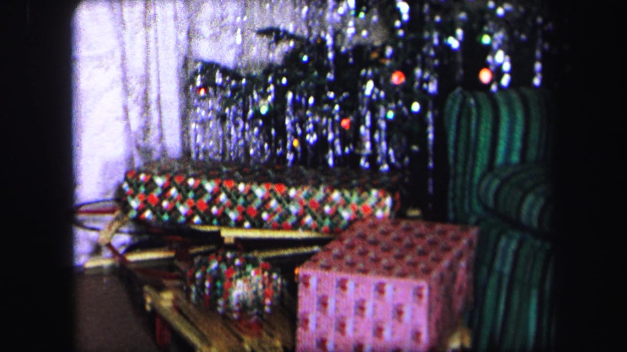 Wrapped gifts under a tinsel Christmas tree beside a green striped chair.