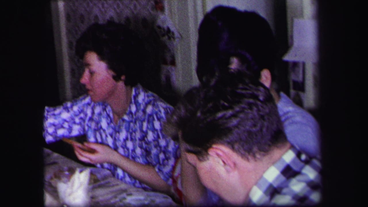 Woman in a blue patterned blouse gestures at the table while a man in a checkered shirt leans forward.