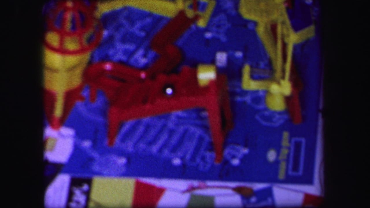 1971 Lynbrook 8mm frame showing a tabletop toy mechanism with a red ramp, yellow parts, blue board surface, and a silver ball bearing.