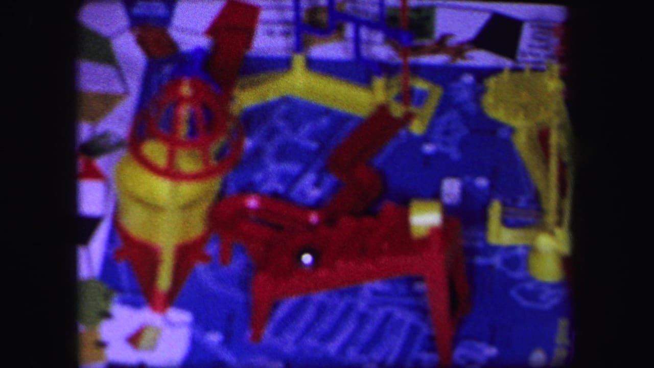 1971 Lynbrook 8mm frame of the toy mechanism from above, showing red levers, yellow supports, a blue board, and a visible ball bearing.