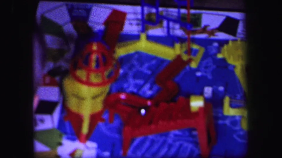 1971 Lynbrook 8mm frame showing a soft-focus close view of the tabletop toy mechanism with bright red, yellow, and blue parts.
