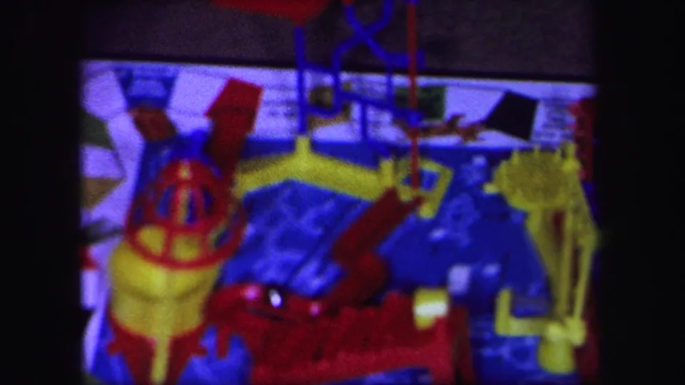 1971 Lynbrook, New York 8mm frame showing a close-up of a colorful mechanical Mouse Trap-style board game with red, yellow, and blue plastic components.