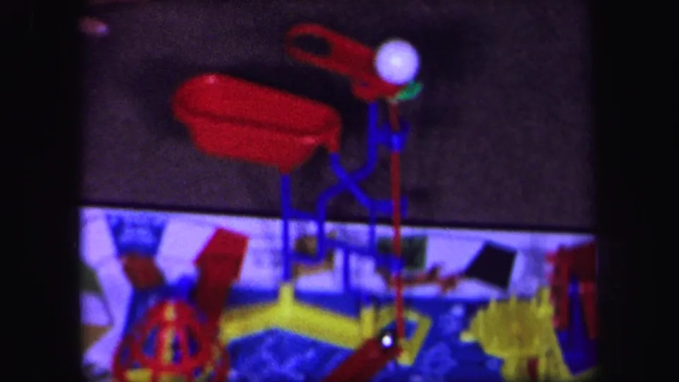 1971 Lynbrook, New York 8mm frame showing a red plastic tub-like component, white ball, and colorful mechanical board game parts near the end of the clip.