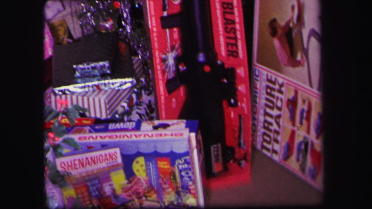 1971 Lynbrook home-movie frame showing wrapped gifts, toy boxes, and holiday tinsel beside a small Christmas tree.