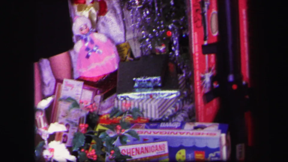 1971 Lynbrook home-movie frame showing toys and wrapped gifts crowded around a decorated Christmas tree indoors.