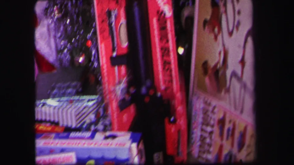 1971 Lynbrook home-movie frame showing a closer view of toy boxes, shiny tinsel, a red toy blaster, and holiday gift packaging.