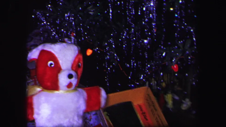 Final 1971 Lynbrook frame with the plush dog partly cropped beside a wrapped present and tinsel-covered Christmas tree.