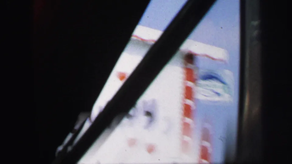 Final 1971 8mm frame with the sign sliding out of view, partly obscured by dark car-window framing and motion blur.