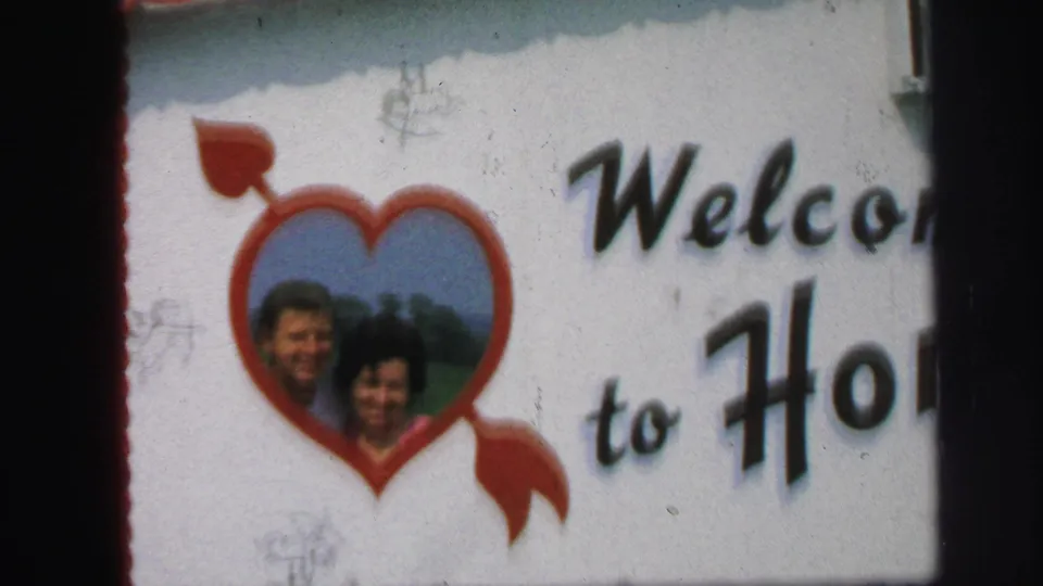 Closer 1971 Lynbrook 8mm view of the red heart portrait on the handmade welcome sign with partial “Welcome” and “to Ho” lettering.