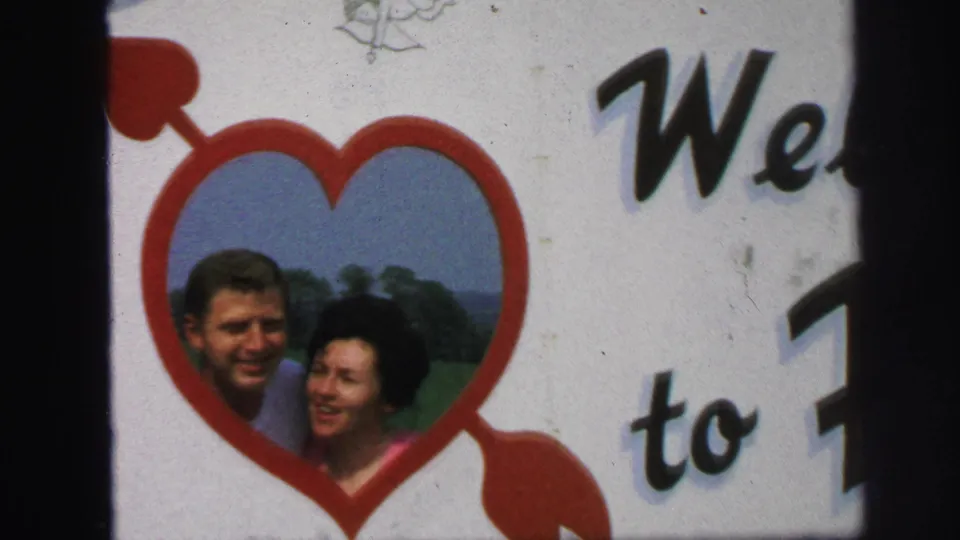 Close 1971 Lynbrook frame of the couple portrait inside a red heart, with partial welcome lettering and visible 8mm film grain.