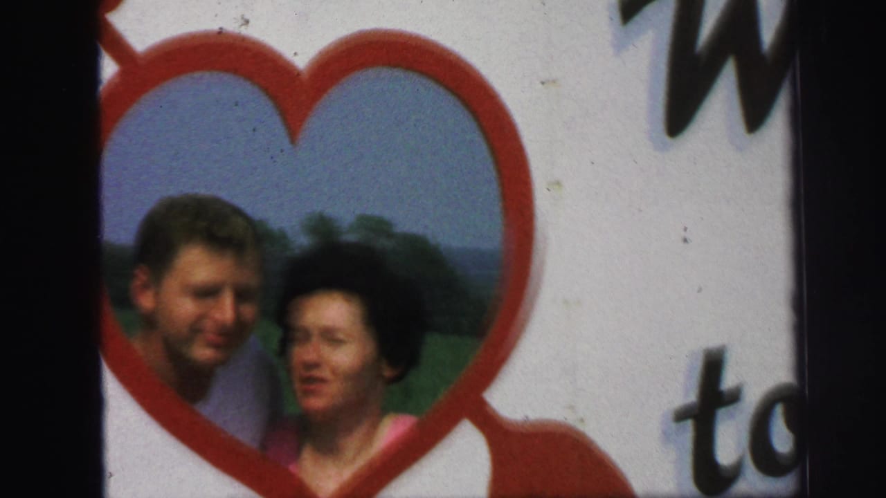 Man and woman pose close together inside a red heart frame.