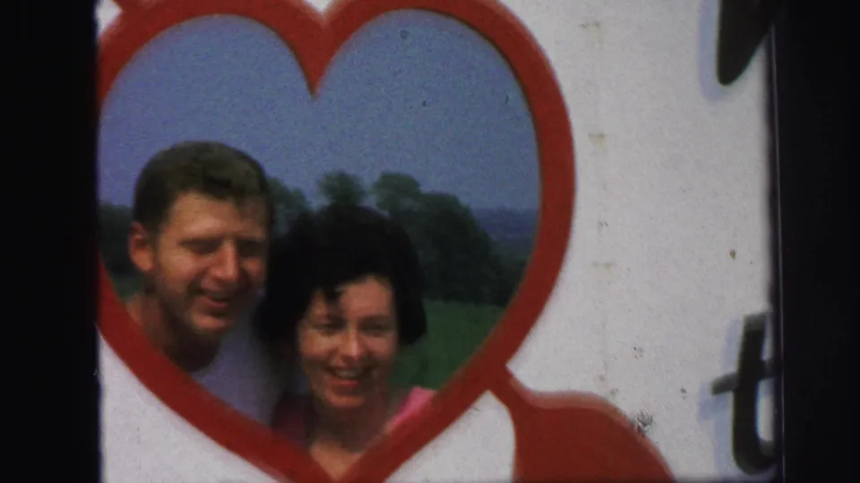 A closer 8mm frame shows the man and woman smiling within the red heart frame, with the outdoor background softened by focus and grain.