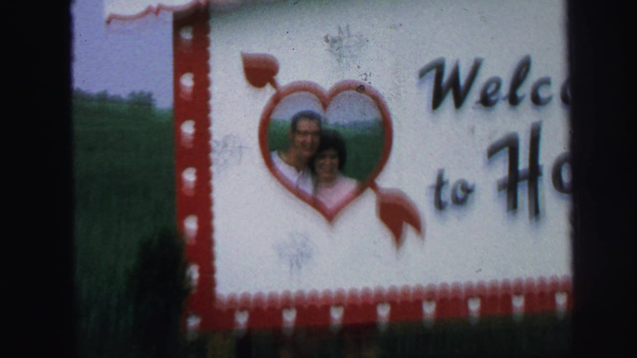The handmade heart welcome sign remains visible, with the adult couple framed inside the heart and the right side of the sign cropped.