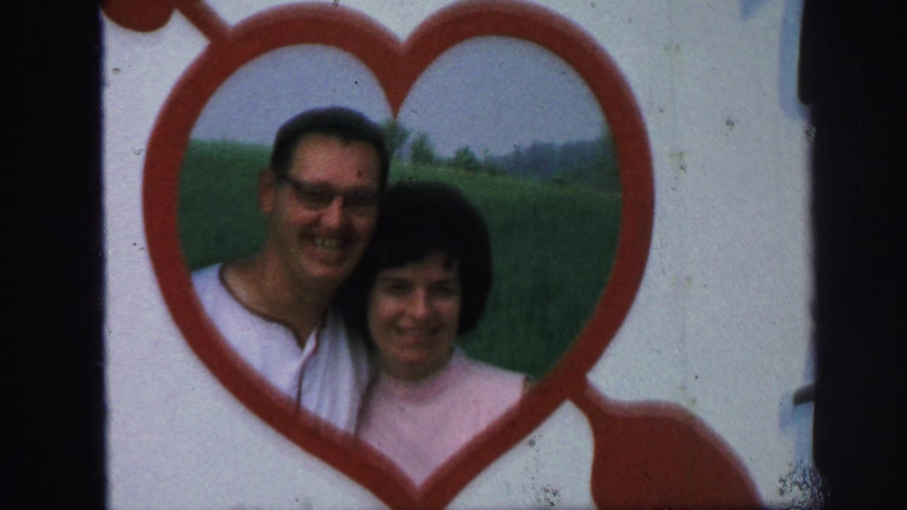 In 1971 Lynbrook home-movie footage, a man in glasses and a woman in a pink top smile inside a large red heart decoration.