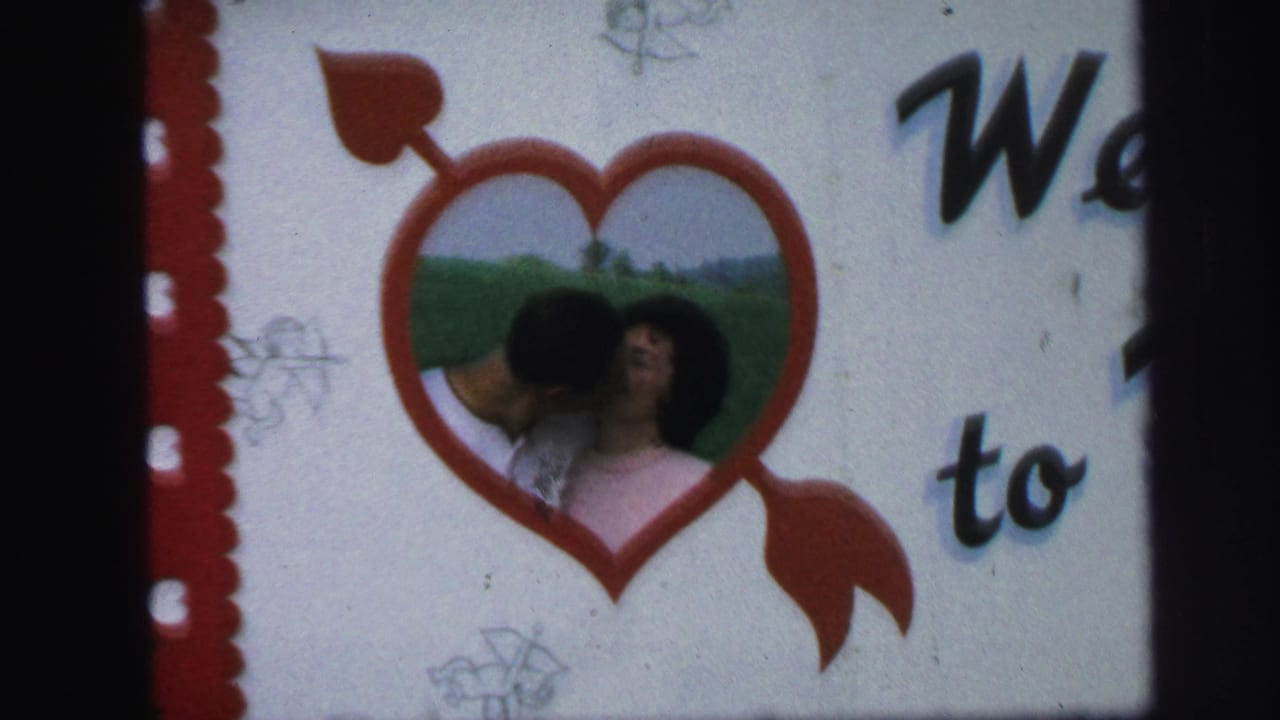 Couple kissing inside a red heart decoration on a white sign.