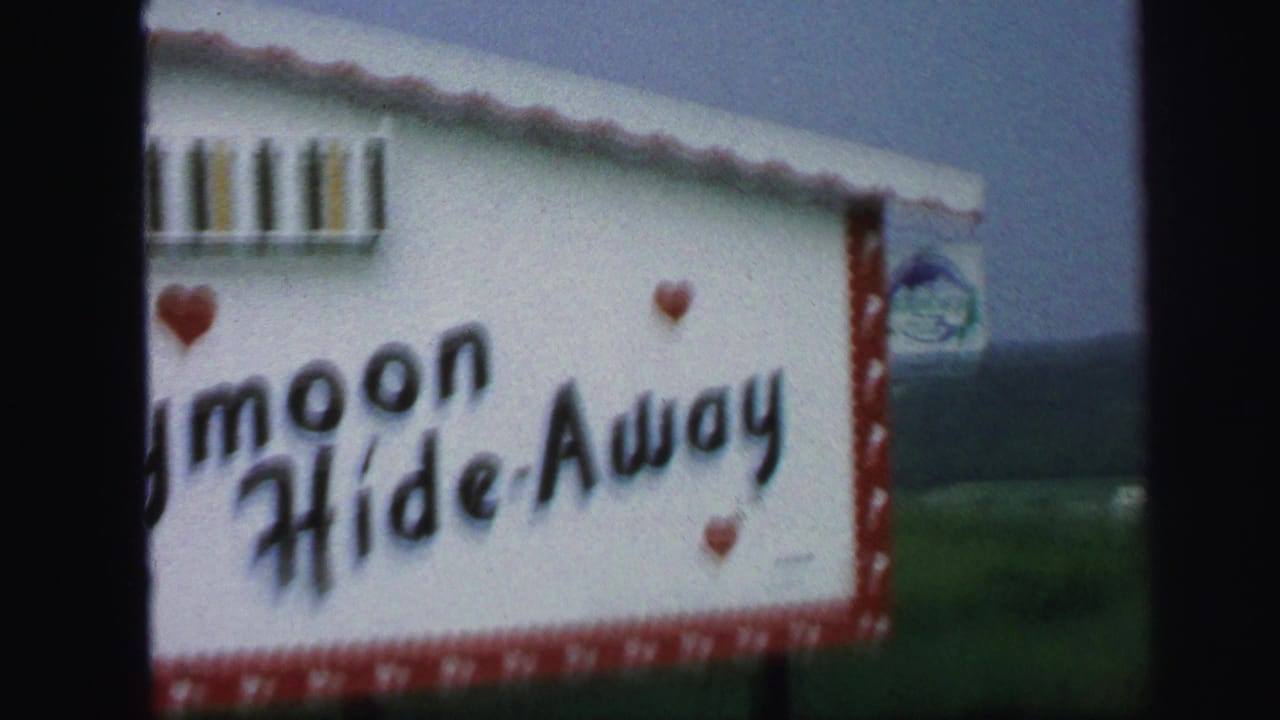 1971 Lynbrook home-movie frame showing a white and red Honeymoon Hide-Away sign, partly cropped, with hearts and dark film edges.