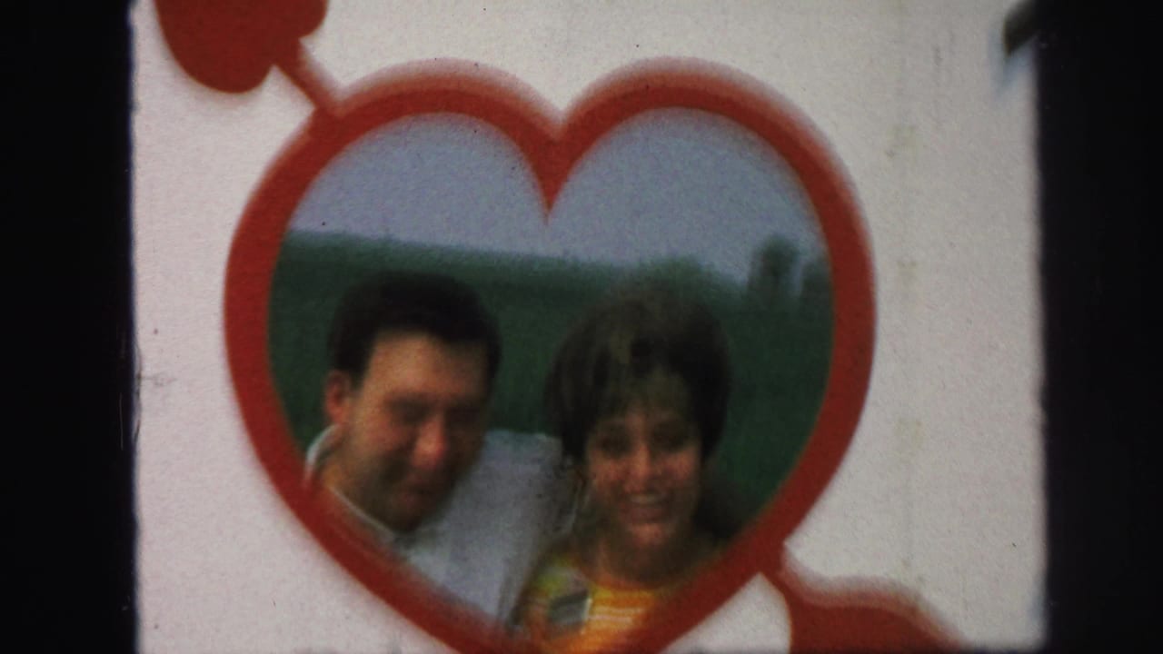 The couple continues posing in the heart-shaped frame, with the soft 8mm image showing faces, red trim, and green landscape.