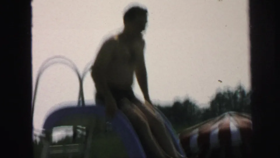 Soft 8mm frame of a boy descending the blue pool slide in a backyard pool area in Lynbrook, New York.