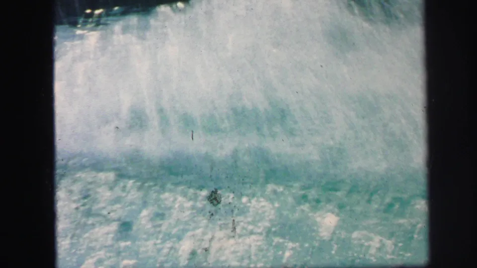 Water erupts in a bright splash at the end of the pool slide action, with grain and exposure shifts from the 8mm scan.