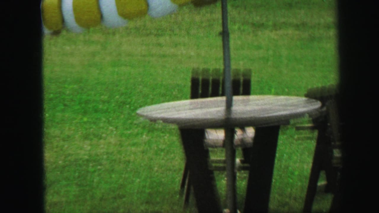 1971 Lynbrook backyard view of a green-and-white striped patio umbrella, outdoor table, and chairs on the lawn.