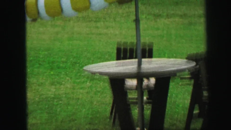 1971 Lynbrook backyard view of a green-and-white striped patio umbrella, outdoor table, and chairs on the lawn.