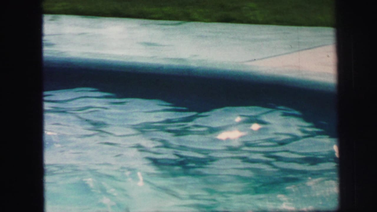 1971 Lynbrook home-movie frame showing sunlit turquoise pool water, a pale concrete edge, and dark 8mm gate borders.