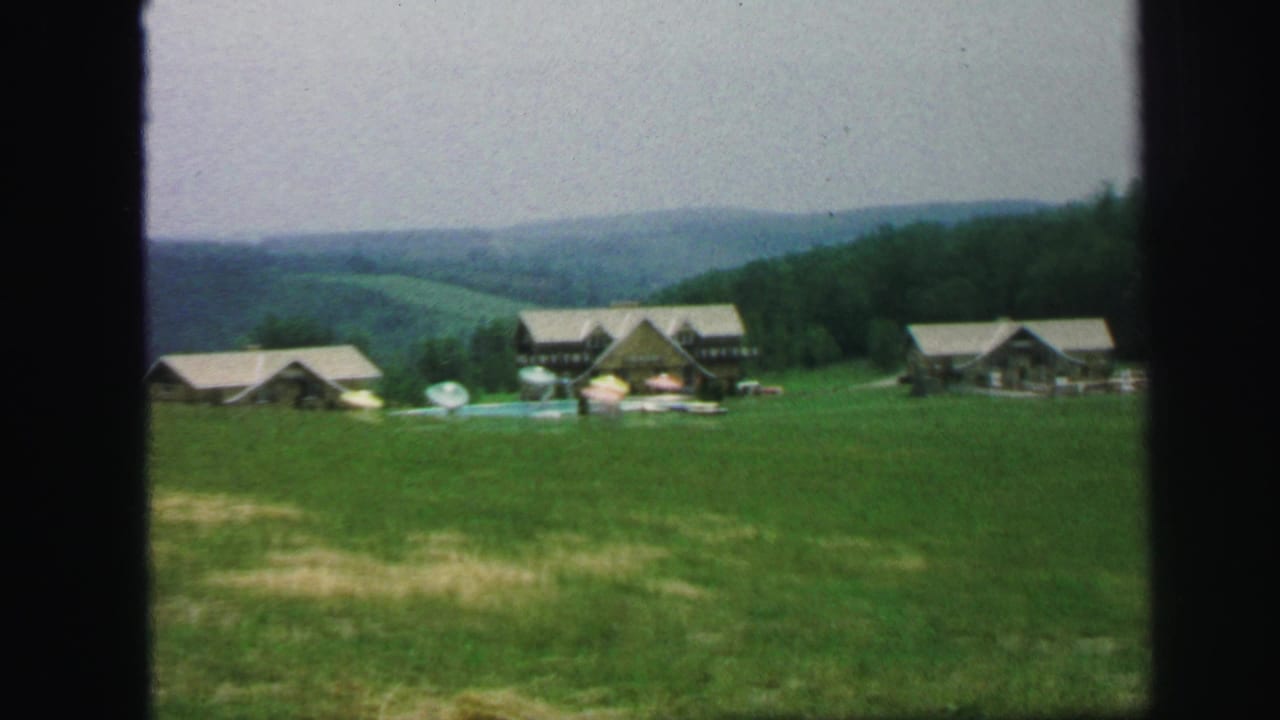 Wide view of lodge buildings and cabins across a grassy slope with wooded hills beyond.