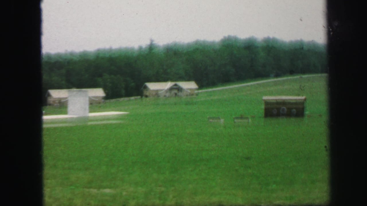 Green field with distant buildings and trees seen through dark film-frame borders.