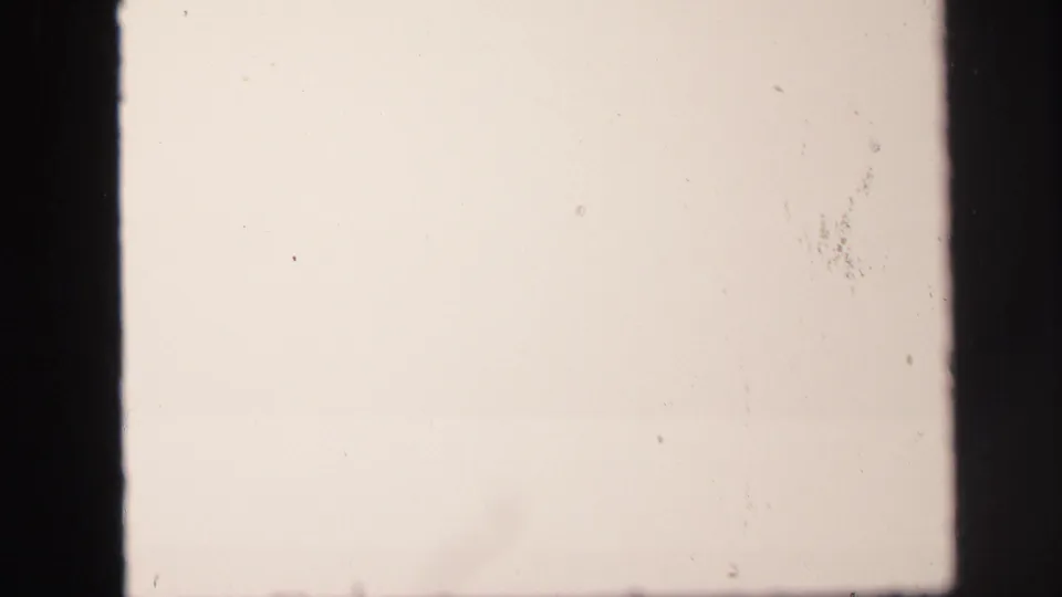 Overexposed 8mm frame from the Lynbrook clip, with a pale blank field, dark projector edges, and visible film dust.