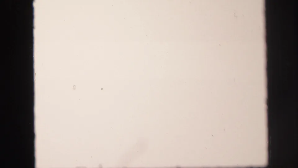 Washed-out 8mm frame with minimal visible detail, dark film borders, and light dust or scratches on the film surface.