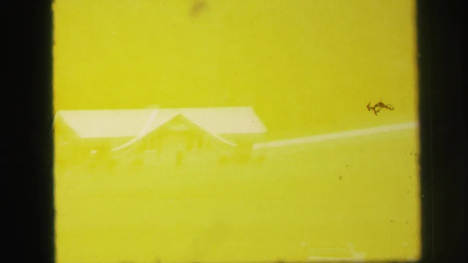 Yellow-flared 1971 Lynbrook frame showing a faint long building or shed roof in open land with heavy exposure tint.